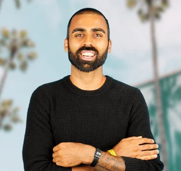 About Us: A bearded man standing in front of a palm tree.